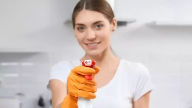 Woman in white top and orange gloves holding a white bottle in her hand.