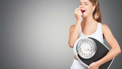 A woman smiles while holding a weight scale, conveying a sense of achievement and positivity about her fitness journey.